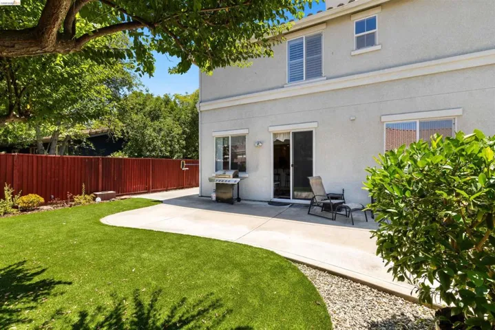 Backyard featuring a concrete patio, artificial turf, a red-stained wooden fence, and mature trees