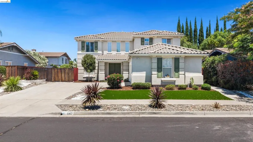 Stucco exterior residence featuring a tile roof, a concrete driveway, and a front yard with artificial turf and decorative rock landscaping