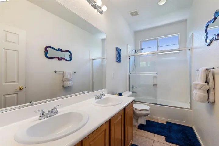 Bathroom featuring a dual vanity with integrated sinks, a chrome faucet, and a light wood-finish cabinet