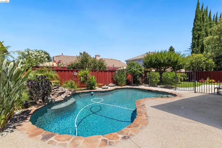 Freeform swimming pool with rock coping and waterfall feature, surrounded by mature landscaping and a concrete patio