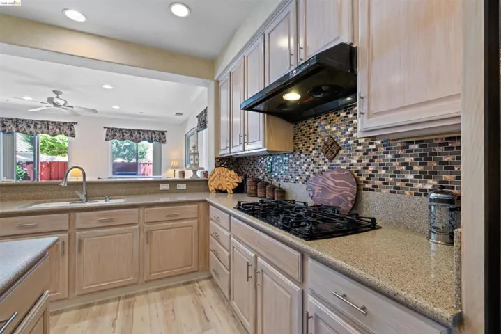 Kitchen featuring a gas range, mosaic tile backsplash, light wood-finish cabinetry, recessed lighting, and a pass-through window with a sink