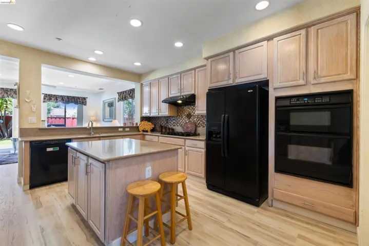 Kitchen featuring a central island with countertop, light wood-finish cabinetry, black appliances, and recessed lighting