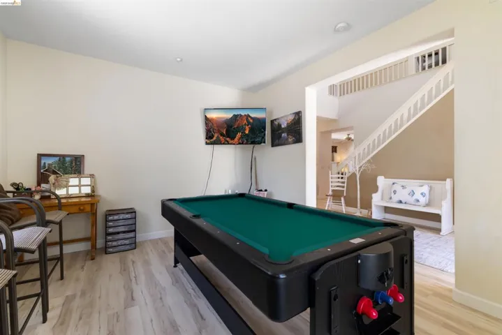 Recreation room featuring a pool table, wall-mounted display, wood-finish flooring, and a white staircase with balusters