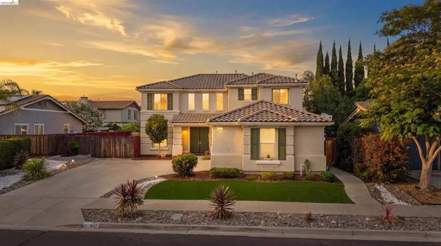 Stucco exterior featuring a tiled roof, green window shutters, and a well-maintained front yard with mature landscaping and decorative rock elements
