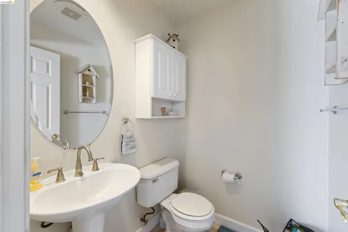 Pedestal sink with brass-finish faucet, oval mirror, wall-mounted white cabinetry, and a toilet