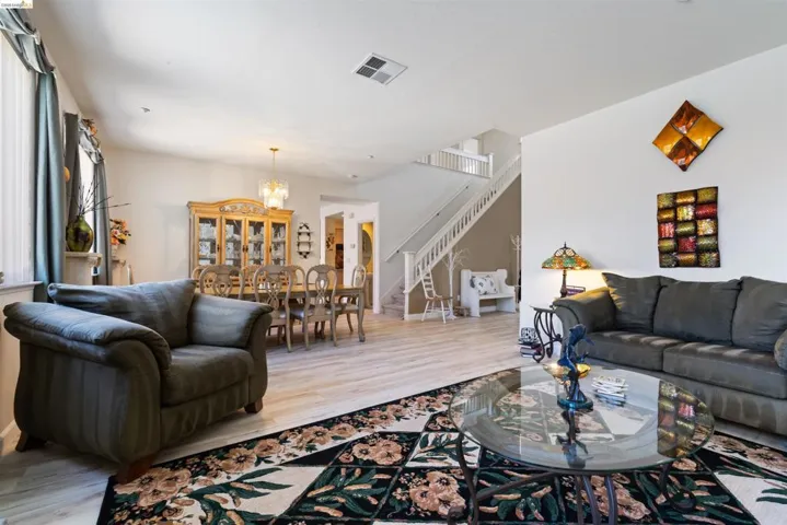 Open-concept living space featuring wood-finish flooring, a contemporary chandelier, and a white staircase with wood railings