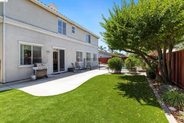 Expansive outdoor living area featuring a concrete patio, artificial turf lawn, mature trees, and a privacy fence
