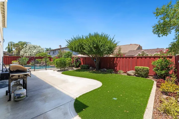 Spacious backyard featuring a concrete patio, a manicured lawn area, and mature landscaping