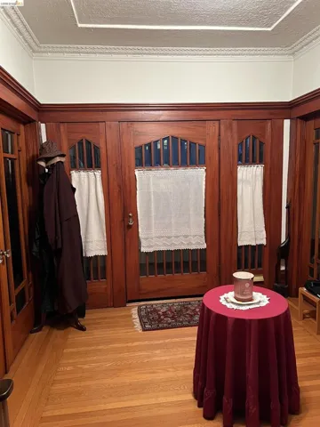 Hardwood flooring entry featuring dark wood trim, matching wood-finish doors with glass panels, and a decorative ceiling molding