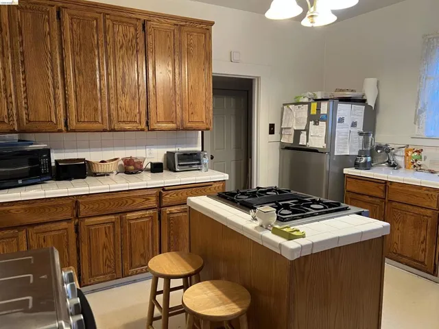 Kitchen featuring wood-finish cabinetry, tile countertops, an island with a built-in cooktop, and tile backsplash
