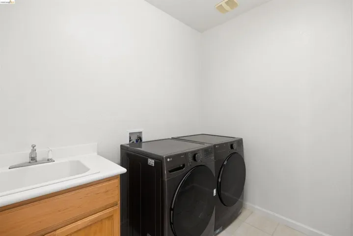 Laundry area featuring a utility sink with a chrome faucet, wood-finish cabinetry, and light-toned floor tile