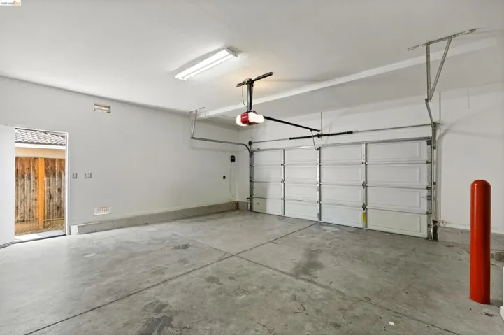 Spacious garage featuring a concrete floor, overhead fluorescent lighting, an automatic garage door opener, and a side entry door