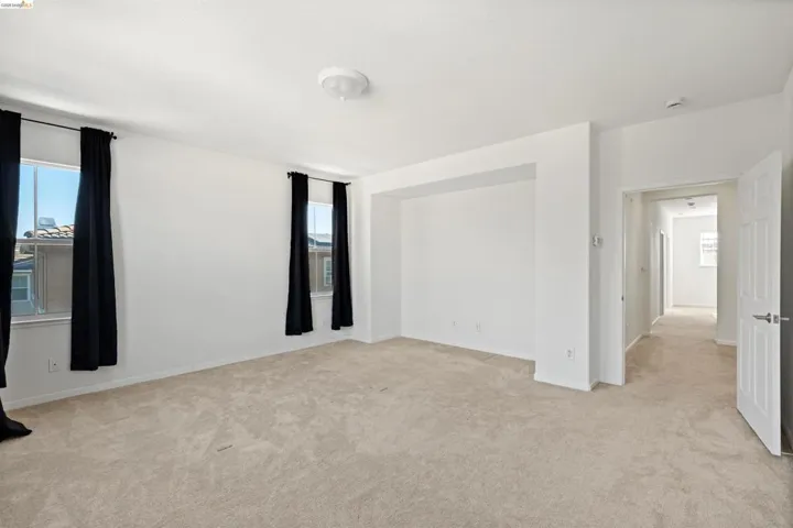 Spacious room featuring light neutral wall paint, warm-toned carpeting, two windows with black drapes, and a built-in wall niche