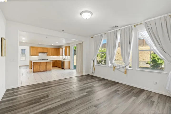 Open concept living area with wood-finish flooring, a kitchen with light wood cabinetry, a center island with a white countertop, and white tile flooring