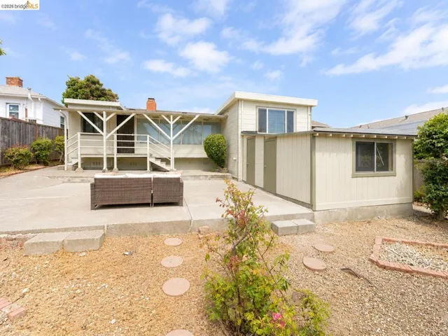 Exterior rear of the property featuring a concrete patio, wood fencing, and an auxiliary structure with dual access doors and a window
