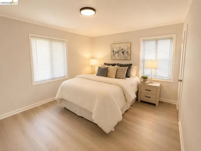 Bedroom featuring light wood-finish flooring, two windows with blinds, a ceiling-mounted light fixture, and crown molding