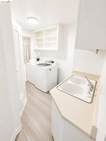 Dedicated laundry area featuring a utility sink with a light-toned countertop, wood-finish flooring, and white cabinetry