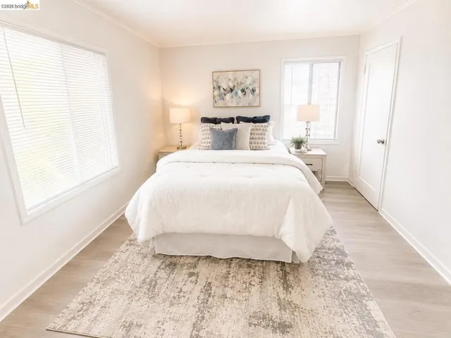 Light-filled room featuring two windows with horizontal blinds, wood-finish flooring, white baseboards, and crown molding
