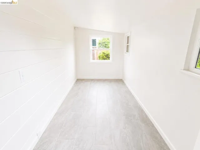 Light-filled interior space featuring three windows, white walls, and light gray tile flooring