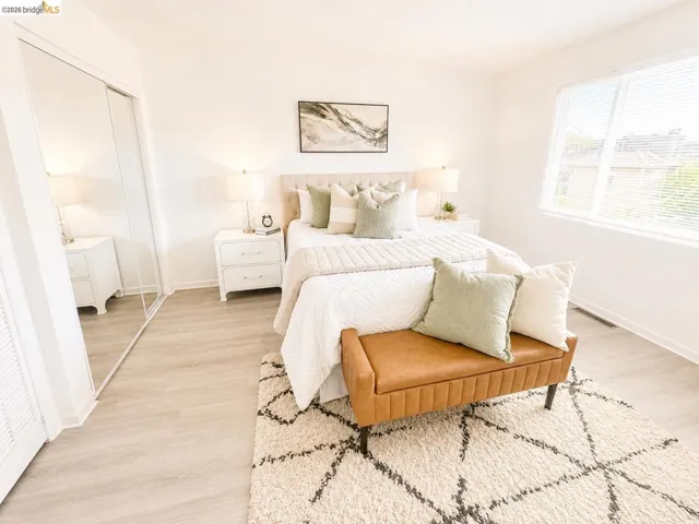 Spacious room featuring light wood-finish flooring, a large window with blinds, and white walls