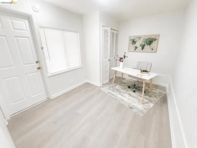 Bright interior space featuring light wood-finish flooring, a panel-style door with brass hardware, a window with horizontal blinds, and louvered bi-fold closet doors