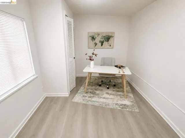 Bright room featuring wood-finish flooring, a window with blinds, and a louvered bifold door