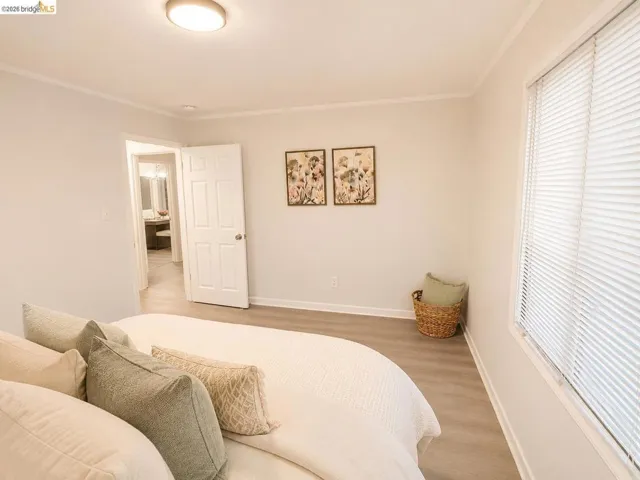 Spacious room featuring light wood-finish flooring, white baseboards, and a large window with horizontal blinds
