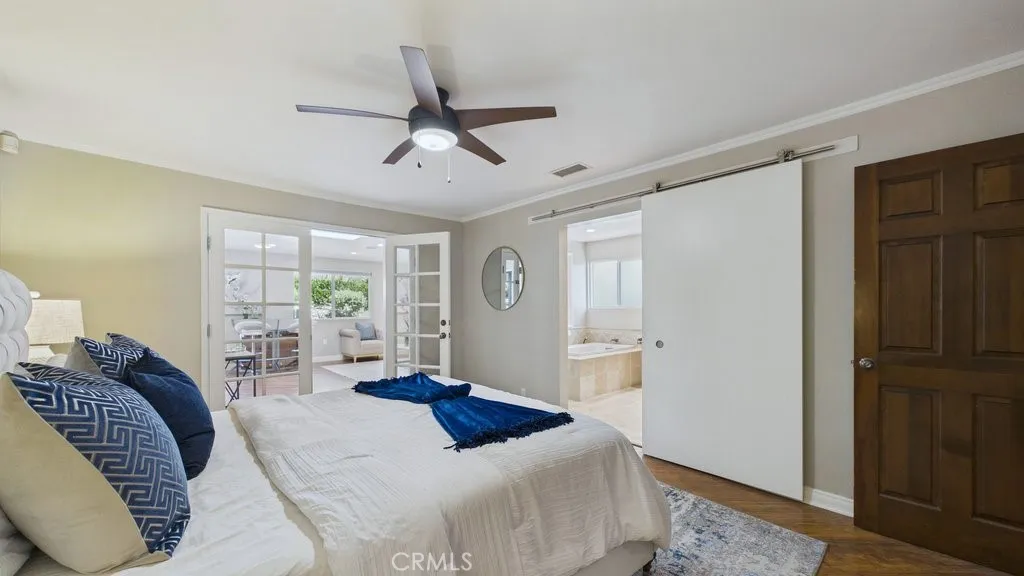 Spacious primary bedroom featuring an en-suite primary bathroom to the right and elegant French doors that open into the family room, providing seamless access to the patio and pool area.