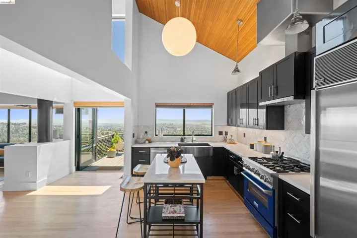 Modern kitchen featuring high ceilings with wood paneling, black cabinetry, stainless steel appliances, and a central island with a light-toned countertop