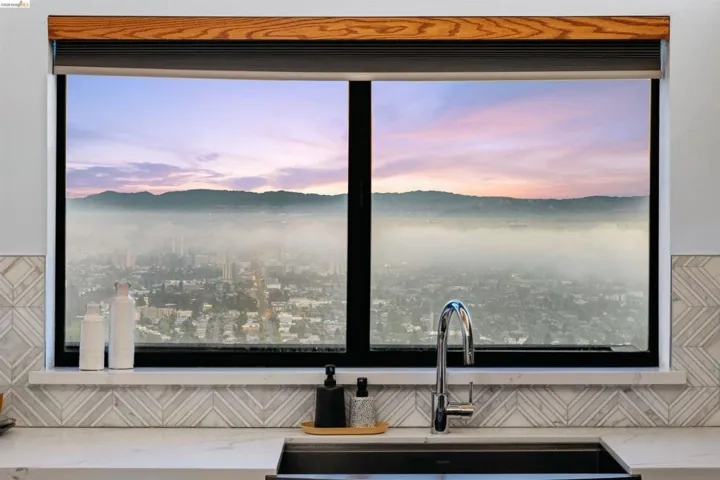 Modern kitchen window featuring a wood-finish valance, roller shade, and a deep undermount sink with a gooseneck faucet