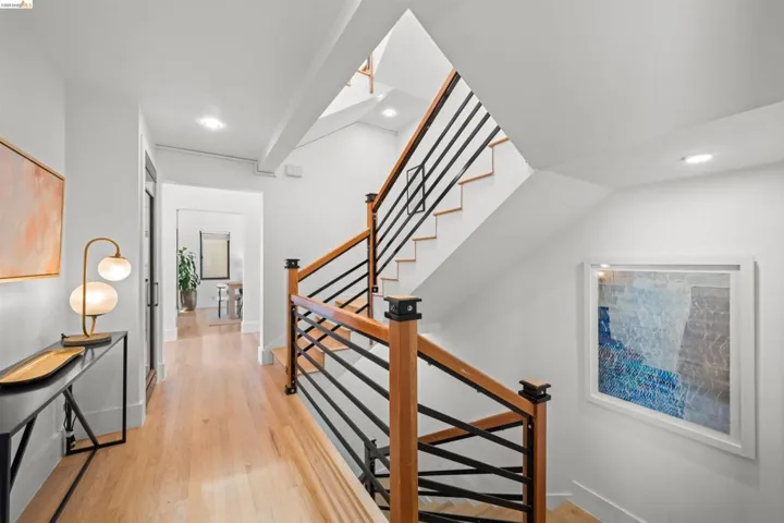Multi-level interior featuring light wood-finish flooring, a contemporary staircase with black metal balusters and wood handrails, recessed lighting, and white walls