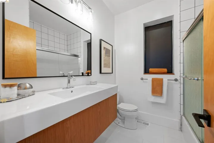 Contemporary bathroom featuring a floating wood-finish vanity with an integrated basin sink, a large framed mirror, and a tiled shower with a frosted glass enclosure