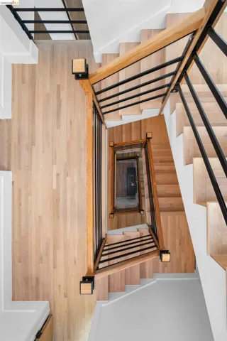Multi-level staircase featuring light wood-finish treads and risers, black metal balusters, and natural wood handrails