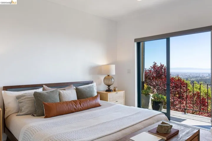 Bright interior space featuring a sliding glass door, a private balcony with metal railings, a natural wood-finish headboard, and recessed lighting