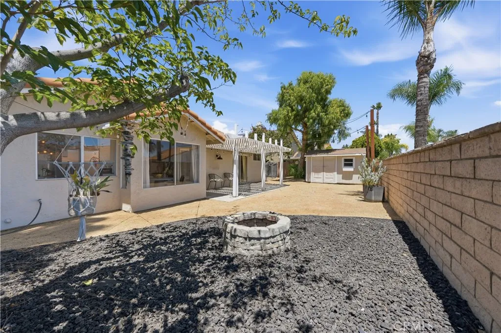 The space offers plenty of room to relax and entertain, featuring a covered pergola, fire pit area, and a detached storage shed.