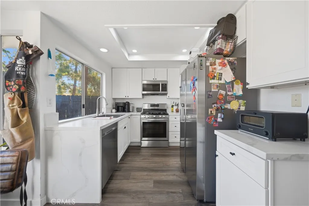 The kitchen features white shaker cabinetry, quartz-style countertops, stainless steel appliances, recessed lighting, and a large window that fills the space with natural light.