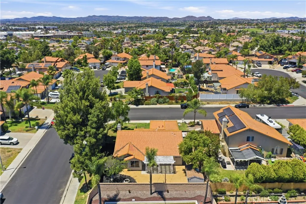 An aerial perspective showcases the property's spacious backyard, corner lot setting, and convenient location within an established neighborhood surrounded by mature trees and mountain views.
