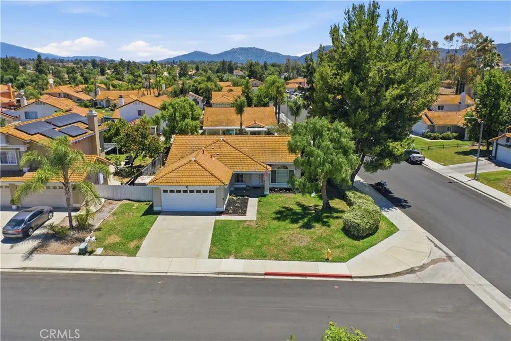 An aerial view highlights the home's desirable corner lot location, mature trees, spacious yard, and scenic mountain views in the distance.