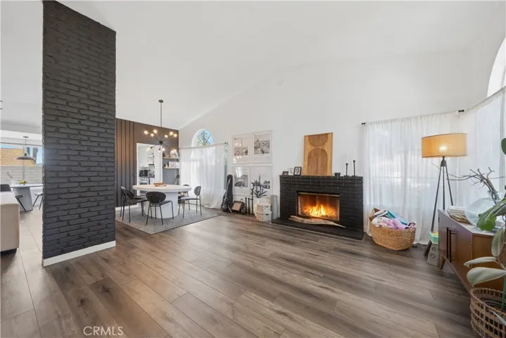 A bright and open living space with vaulted ceilings, updated flooring, and a striking brick fireplace as the focal point.