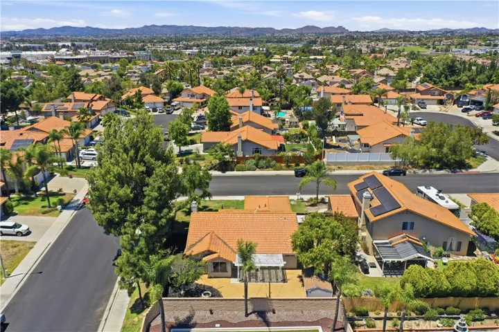 An aerial perspective showcases the property's spacious backyard, corner lot setting, and convenient location within an established neighborhood surrounded by mature trees and mountain views.