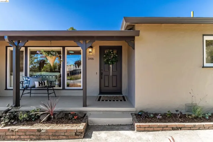Front exterior featuring a covered porch with dark wood columns and beams, stucco siding, and a dark paneled entry door