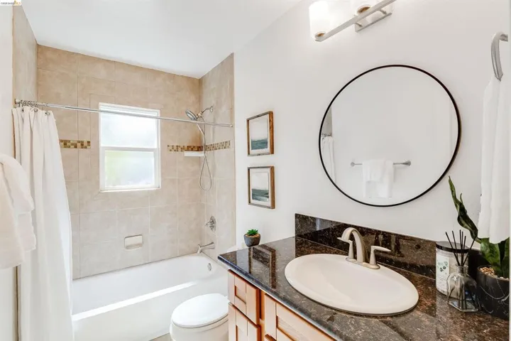 Bathroom featuring a single vanity with stone-finish countertop, undermount sink, and a circular mirror