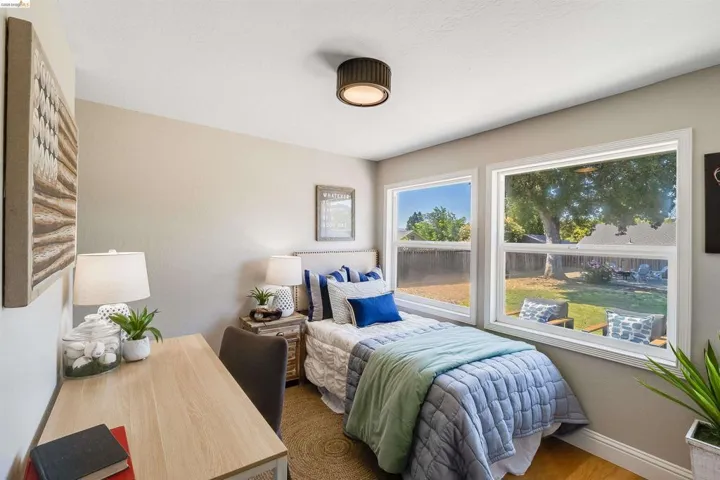 Bedroom featuring hardwood-finish flooring, two large windows, a neutral wall color, and a modern drum ceiling light fixture