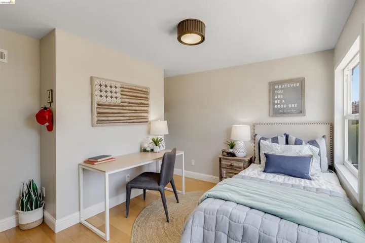 Bedroom featuring light wood-finish flooring, neutral wall tones, a large window, a ceiling-mounted light fixture, and white baseboards