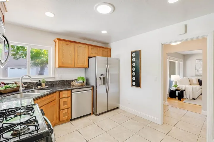 Kitchen featuring granite countertops, stainless steel appliances, wood cabinetry, tile flooring, and recessed lighting