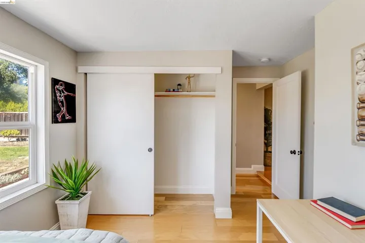 Bedroom featuring a large window, light wood-finish flooring, a white sliding barn door closet, an interior doorway, and neutral wall tones