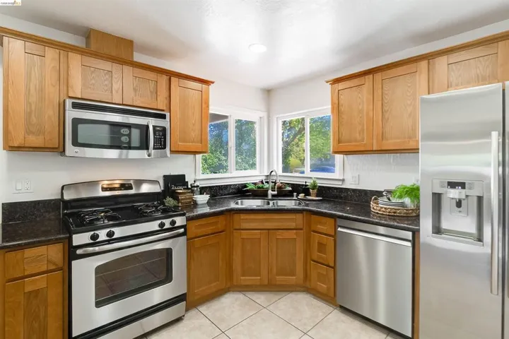 Kitchen featuring wood cabinetry, stainless steel appliances, dark countertops, and tile flooring