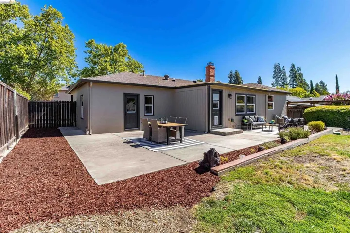 Rear exterior featuring a concrete patio, wood fencing, and a raised planter bed