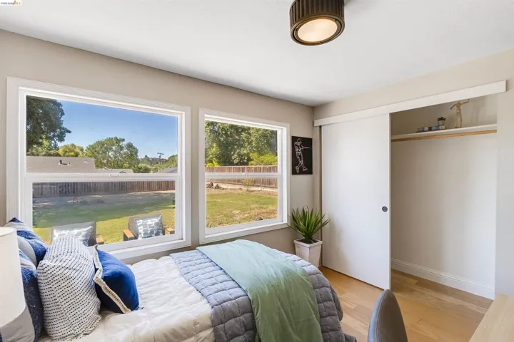 Bedroom featuring two large windows, sliding closet doors, wood-finish flooring, a contemporary ceiling light fixture, and baseboard molding