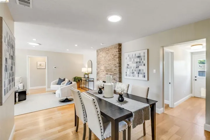 Open-concept living space featuring light wood-finish flooring, recessed lighting, a stone accent wall, and a bright white door